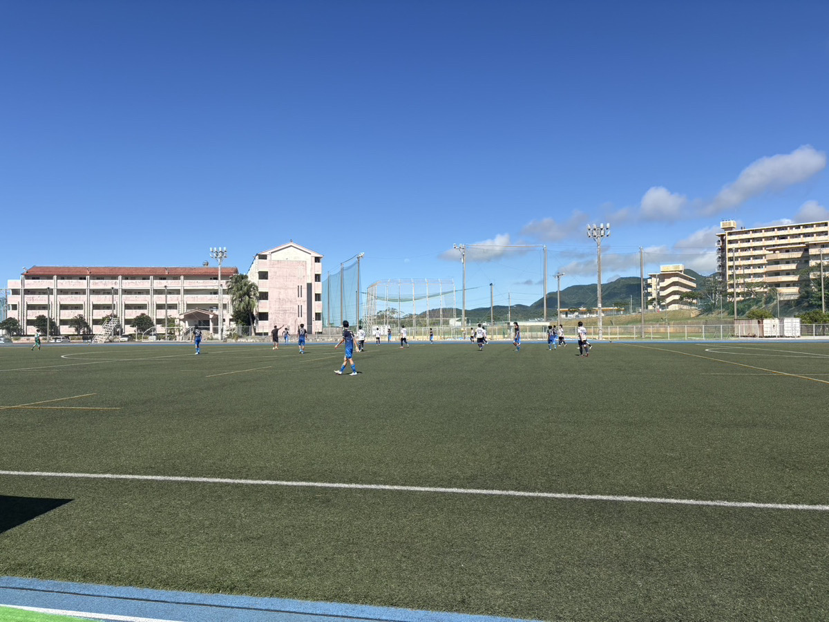 青空の下に広がる人工芝グラウンドと、試合中の選手たち