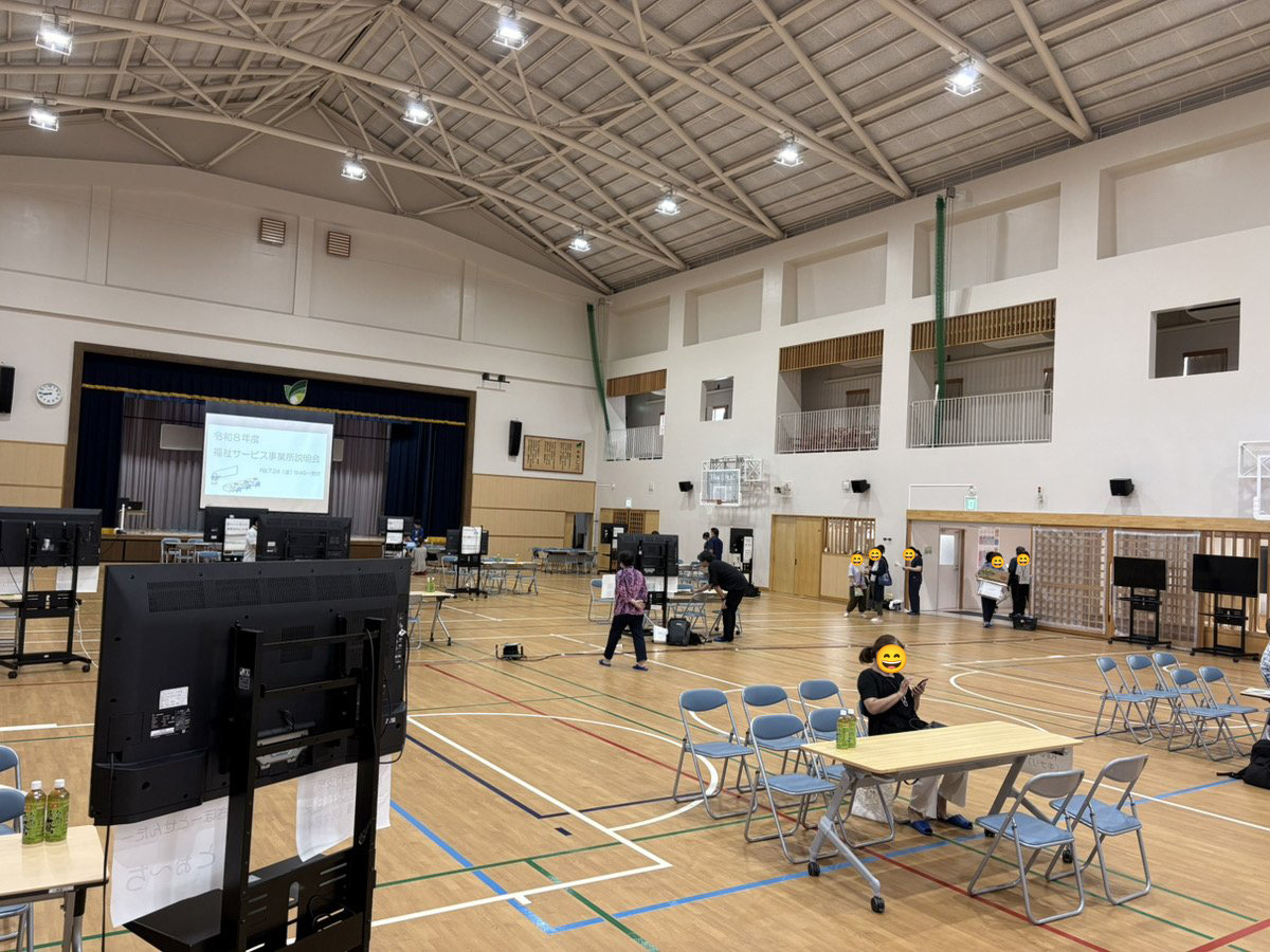 開場前の体育館で各事業所がモニターや資料を設営している様子