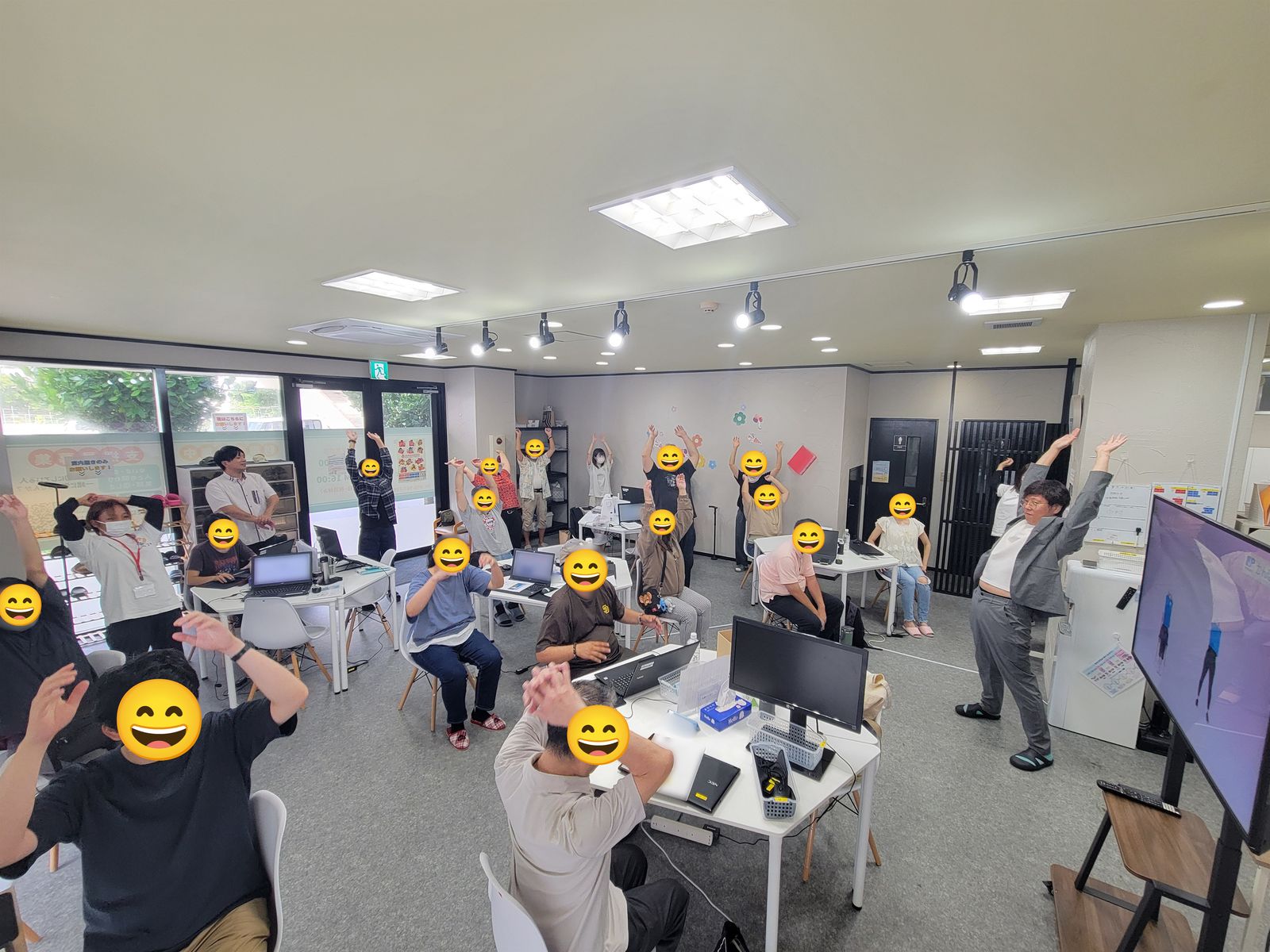 立って体操する利用者さんと、椅子に座ったまま腕を動かす利用者さんがいる、みらコラボ那覇市三原の事業所内の様子