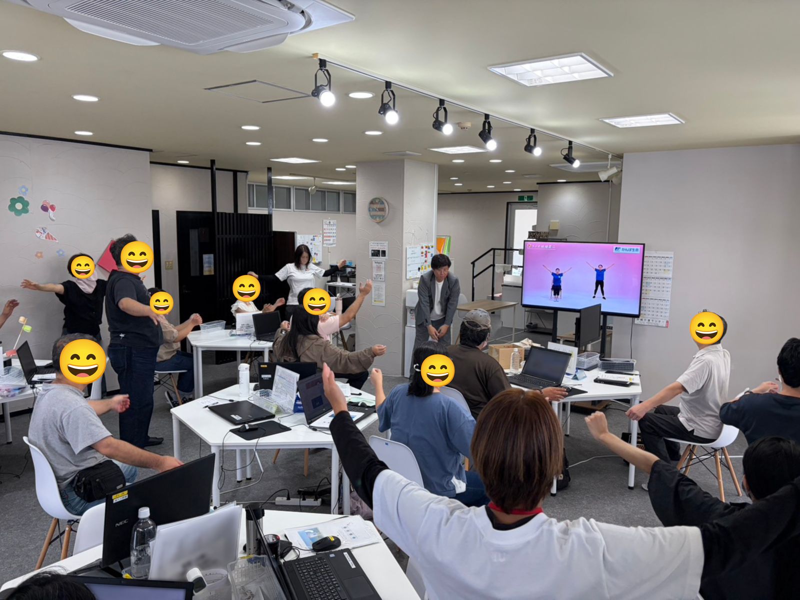 ノートパソコンが置かれた机の前で、利用者さんたちが腕を伸ばして体操している様子