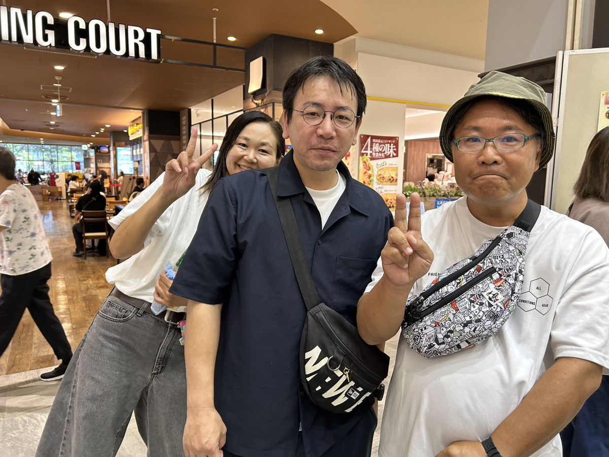こころの健康フェスタの会場で、ピースサインをして記念撮影する、みらコラボの友利と、国場本店の元利用者さん、利用者さん